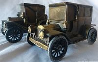 Front angled view of two vintage metal car piggy banks, showing details and relative sizes.