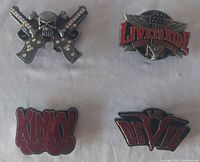 Top view of all four belt buckles showing designs including skull with crossed guns, Live to Ride with wings, Kinky, and Lil Devil