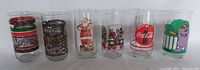 All six Coca Cola themed glasses lined up together showing variety of holiday and vintage designs, including Santa and Grimace characters
