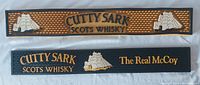 Front view of two Cutty Sark bar mats: one yellow with ships and text, one black with ships and text 'The Real McCoy'