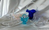 Five decorative glass candy dishes and baskets arranged on a fabric background showing overall lot content.