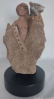 Front view capturing woman and tiger figures emerging from rocky textured base