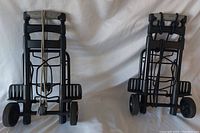 Two Samsonite luggage dollies upright against a white background, showing both dollies side by side with visible wheels, handles, and securing straps.
