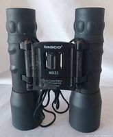 Front view of Tasco binoculars showing 16x32 magnification marking and central focus wheel with some corrosion on the central hinge.