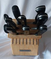 Knife block set showing multiple knives with black handles and triple rivets inserted in wooden block with KitchenAid plaque.