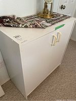 White finish MDF cabinet with two doors closed, cream handles, and decorative cloth on top.