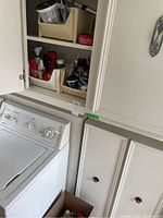 Partial view of cabinet with washing machine visible underneath showing cabinet door open with some bottles inside.