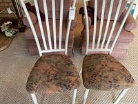 Pair of white metal frame chairs with high vertical slat backs and cushioned seats covered in a patterned cloth showing geometric and floral designs.