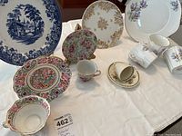 Display of blue Wallace Cimson & Co. collector plate with Swiss Cottage design, Royal Grafton crocus pattern plate with 3 matching cups, and multiple teacups and saucers arranged on a table