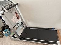 Full side view of silver and black compact treadmill showing running belt, side rails, and partially folded upright frame.