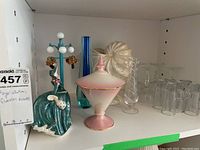 Shelf display showing ceramic shell vase, pink and white Royal Winton lidded container, ceramic figurine, and several glass vases and glasses.