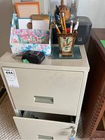 Front view of the beige metal file cabinet with open bottom drawer, floral desk organizer and floral metal pencil holder with pens and pencils on top.
