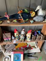Display of garden gnomes, birdhouses, and various animal figurines arranged on shelves and floor, showing scale and variety of items.
