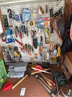 Wide view of pegboard with hanging hand tools and assorted items, workbench surface with tools including wooden mallet, hammer, and saws