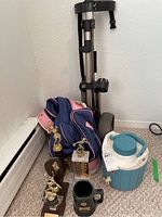 Photo shows pink and navy blue golf bag, metallic golf caddy, blue and white Coleman water cooler, four sports trophies, and ceramic mug.