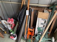 Photo showing the Black & Decker hedge trimmer blade, sprinkler wand, green watering can, box, and various wooden-handled garden tools.