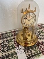 Full view of Kundo anniversary clock under glass dome placed on decorative woven table runner