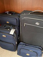Group photo of four pieces of luggage, two navy blue and one large black suitcase, plus a small navy laptop bag.