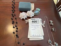 Photo of sterling silver necklace with black beads, bag, ring, earrings, and fabric brooches on wood surface.