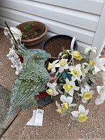 View of green metal bird garden figure, white faux flowers, and multiple outdoor pots arranged outside on patio or concrete surface.