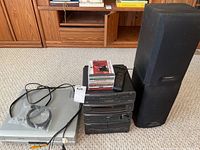 Stereo system with main unit, stack of CDs on top, remote control, and one speaker