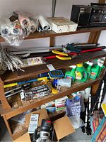 Wooden shelving unit holding assorted gardening tools, paint supplies, mop, gardening chemicals, and a Crown stereo recorder.