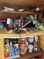 Photo of shelf containing Sears Sabre Saw in box, Black & Decker finishing sander, wood stain cans, spray bottles, and assorted hardware.