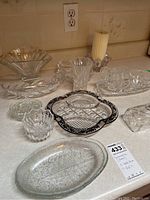Full view of assorted cut glass servingware items including bowls, plates, creamer, sugar bowl, and cups arranged on a countertop.