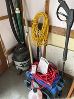 Photo showing Shop Vac wet/dry vacuum, yellow coiled extension cord hanging and part of the pressure washer with a red cord coiled on top.