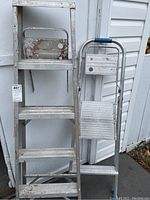Full view of the two ladders side by side, showing their difference in height and condition with paint marks and rust.