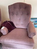 Front view of the chair showing the mauve/dusty rose corduroy upholstery with a striped pillow on the left armrest.