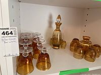 Wide view of yellow glass decanters and multiple glasses in two styles: taller stemmed wine glasses and shorter rounded glasses with gold rims.