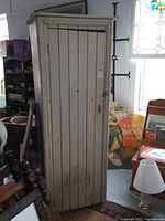 Front view of antique chimney cabinet showing single vertical slatted door with metal handle and aged white paint.