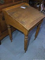 Front angled view of the antique solid wood lift top desk showing the tilt top and turned legs.