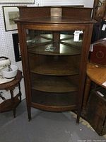 Front view of solid oak corner display cabinet with curved glass door and interior shelves visible.