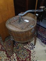 Front side view of antique wooden barrel washing machine showing hand crank and top lid with aged wood.