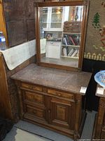 Front view of antique wooden washstand with marble top and matching separate wall mirror behind it.