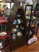 Front view of dark wood canoe-shaped display shelf with glass shelves and bottom cabinet.
