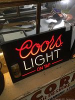 Front view of the illuminated Coors Light On Tap sign with red and white lighting and an attached Miller Genuine Draft can.