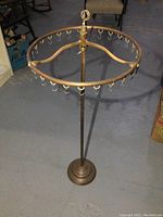 Full view of copper and brass circular frame rotisserie hanger with multiple hooks and cast iron base, standing on floor