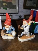 Photo showing both gnome figurines side by side on a table with background artwork.