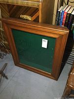 Full front view of the shadow box frame showing the wooden frame and green felt backing inside, door closed.