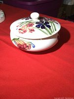 Side and lid view of the round covered dish with floral decorations on the white ceramic.