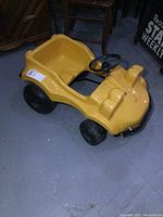 Side angled view showing yellow plastic body with black wheels and metal frame undercarriage