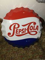 Front view of metal Pepsi-Cola bottle cap sign showing the red, white, and blue color pattern and logo.