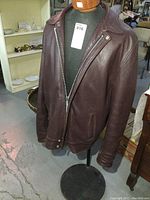 Front view of vintage brown leather jacket with zipper closure on black mannequin torso.