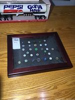 Closed front view of the hinged wooden shadow box displaying a collection of golf ball marker pins on a black mesh background.
