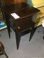 Side and angled front view of vintage solid wood smokers stand showing dark finish, single door with brass knob, tapered legs and minor wear.