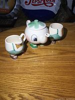 Full set on wooden tabletop showing teapot with matching cream and sugar containers, each with boot feet and whimsical painted design.