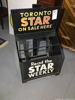 Front view of black metal rack with Toronto Star branding, showing display compartments and promotional text.